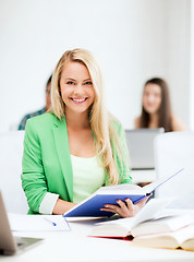 Image showing smiling young woman reading book at school