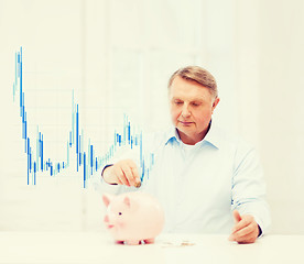 Image showing old man putting coin into big piggy bank
