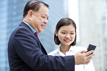 Image showing Asian businessman and young female executive looking at smart phone