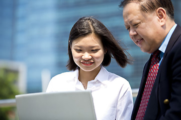 Image showing Asian businessman and young female executive looking at laptop