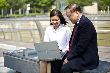 Image showing Asian businessman and young female executive looking at laptop