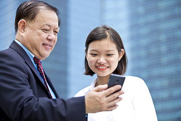 Image showing Asian businessman & young female executive looking at smart phone