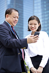 Image showing Asian businessman and young female executive looking at smart phone