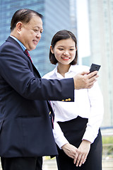 Image showing Asian businessman and young female executive looking at smart phone