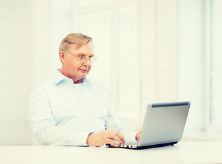 Image showing old man in eyeglasses working with laptop at home