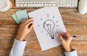 Image showing close up of hands drawing lighting bulb on paper