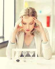 Image showing tired woman behind the table with hourgalss