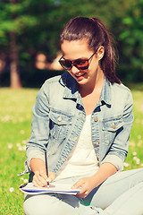 Image showing smiling young girl with notebook writing in park