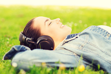 Image showing smiling young girl in headphones lying on grass