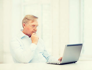 Image showing old man in eyeglasses working with laptop at home