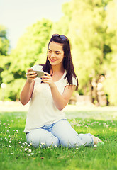 Image showing smiling young girl with smartphone sitting in park