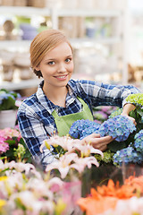 Image showing happy woman taking care of flowers in greenhouse