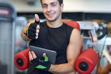 Image showing young man with tablet pc showing thumbs up in gym