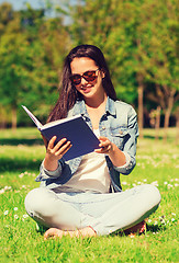 Image showing smiling young girl with book sitting in park