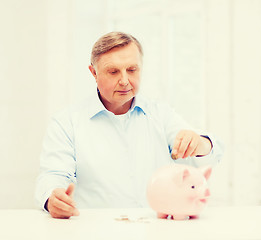 Image showing old man putting coin into big piggy bank