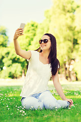 Image showing smiling young girl with smartphone sitting in park