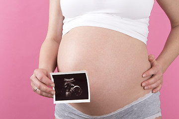 Image showing Closeup of a pregnant woman with an ultrasound picture in her ha