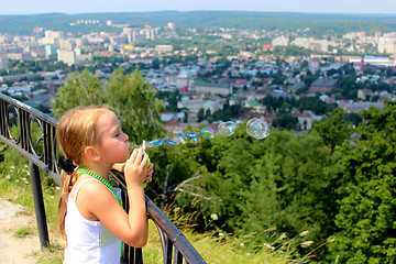 Image showing little girl swelling soap bubbles out of city