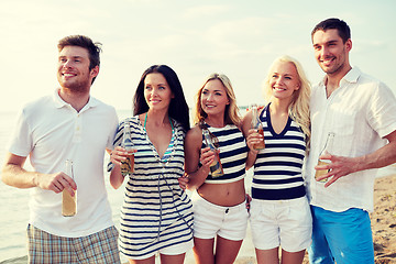 Image showing smiling friends with drinks in bottles on beach