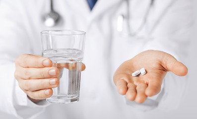 Image showing doctor hands giving white pills and glass of water