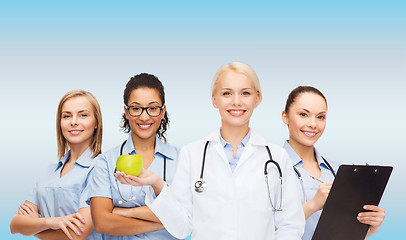 Image showing smiling female doctor and nurses with green apple