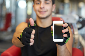 Image showing young man with smartphone showing thumbs up in gym