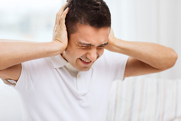 Image showing unhappy man closing his ears by hands at home