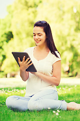 Image showing smiling young girl with tablet pc sitting on grass