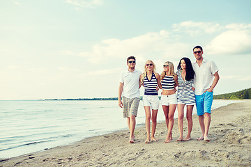 Image showing smiling friends in sunglasses walking on beach