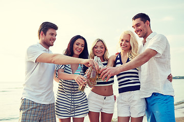 Image showing smiling friends clinking bottles on beach