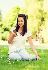 Image showing smiling young girl with smartphone sitting in park