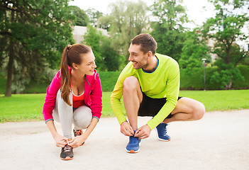 Image showing smiling couple tying shoelaces outdoors