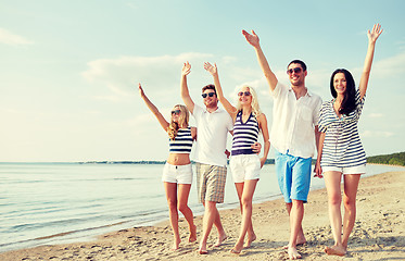 Image showing smiling friends walking on beach and waving hands