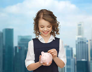 Image showing happy girl putting coin into piggy bank