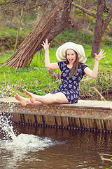 Image showing Cheerful fashionable woman sits on small bridge and splashing water