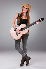 Image showing The beautiful girl in a cowboy\'s hat and acoustic guitar.