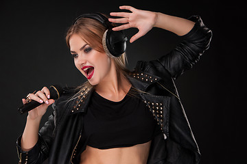 Image showing Portrait of a beautiful woman singing into microphone with headphones in studio on black background
