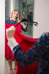 Image showing Woman trying red dress shopping for clothing. 