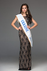 Image showing Beautiful young brunette woman with her hair posing in a i long dress. Studio, on gray background