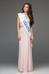 Image showing Beautiful young brunette woman with her hair posing in a i long dress. Studio, on gray background