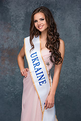 Image showing Beautiful young brunette woman with her hair posing in a i pink dress. Studio, on gray background