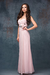 Image showing Beautiful young brunette woman with her hair posing in a i long pink dress. Studio, on gray background