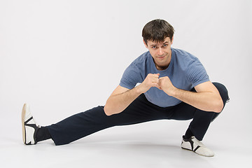 Image showing Athlete crouching stretches the muscles of right leg