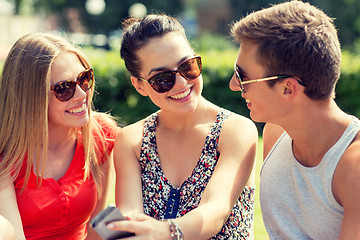 Image showing smiling friends with smartphone sitting in park