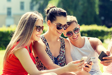 Image showing smiling friends with smartphones sitting in park