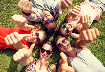 Image showing smiling friends showing thumbs up lying on grass