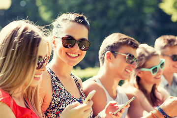 Image showing smiling friends with smartphones sitting in park