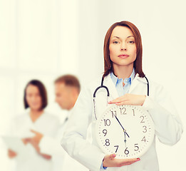 Image showing calm female doctor with wall clock