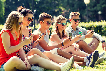 Image showing smiling friends with smartphones sitting on grass