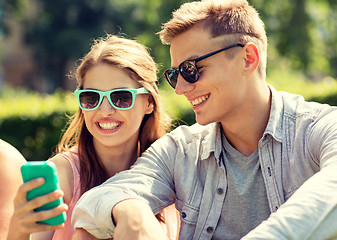 Image showing smiling friends with smartphone sitting in park